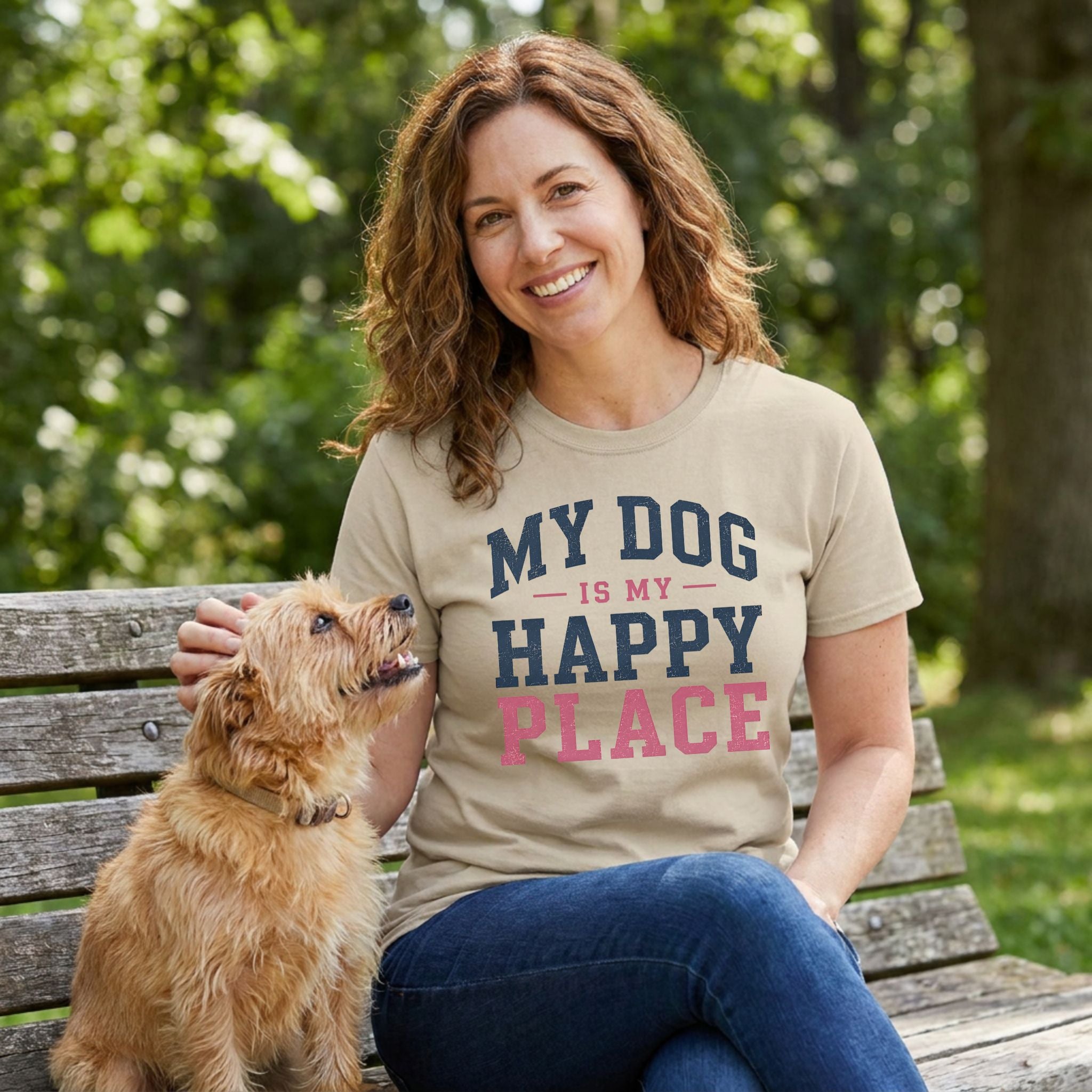 Woman wearing a tan crewneck t-shirt with My Dog Is My Happy Place text, sitting on a park bench with a small terrier.