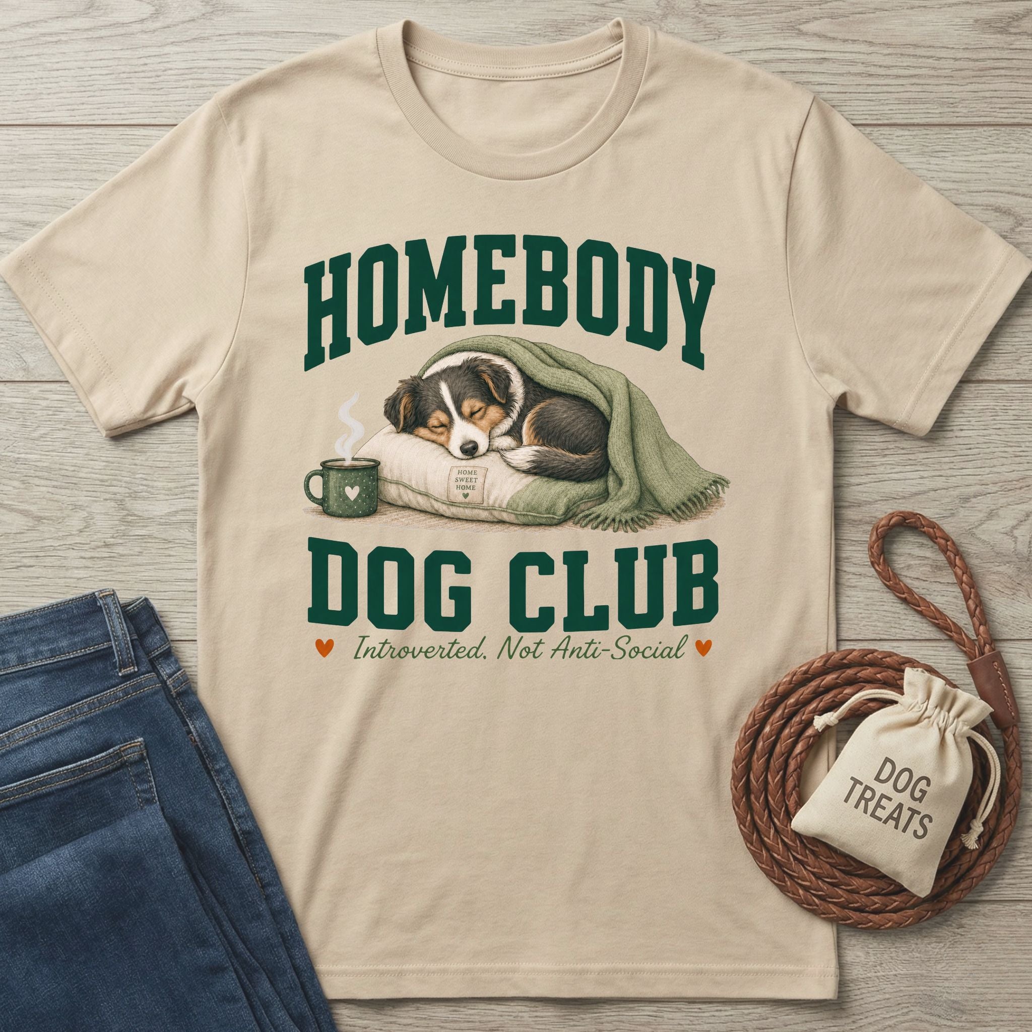 Beige crewneck t-shirt featuring a sleeping dog graphic, green collegiate text, and a cozy homebody design.