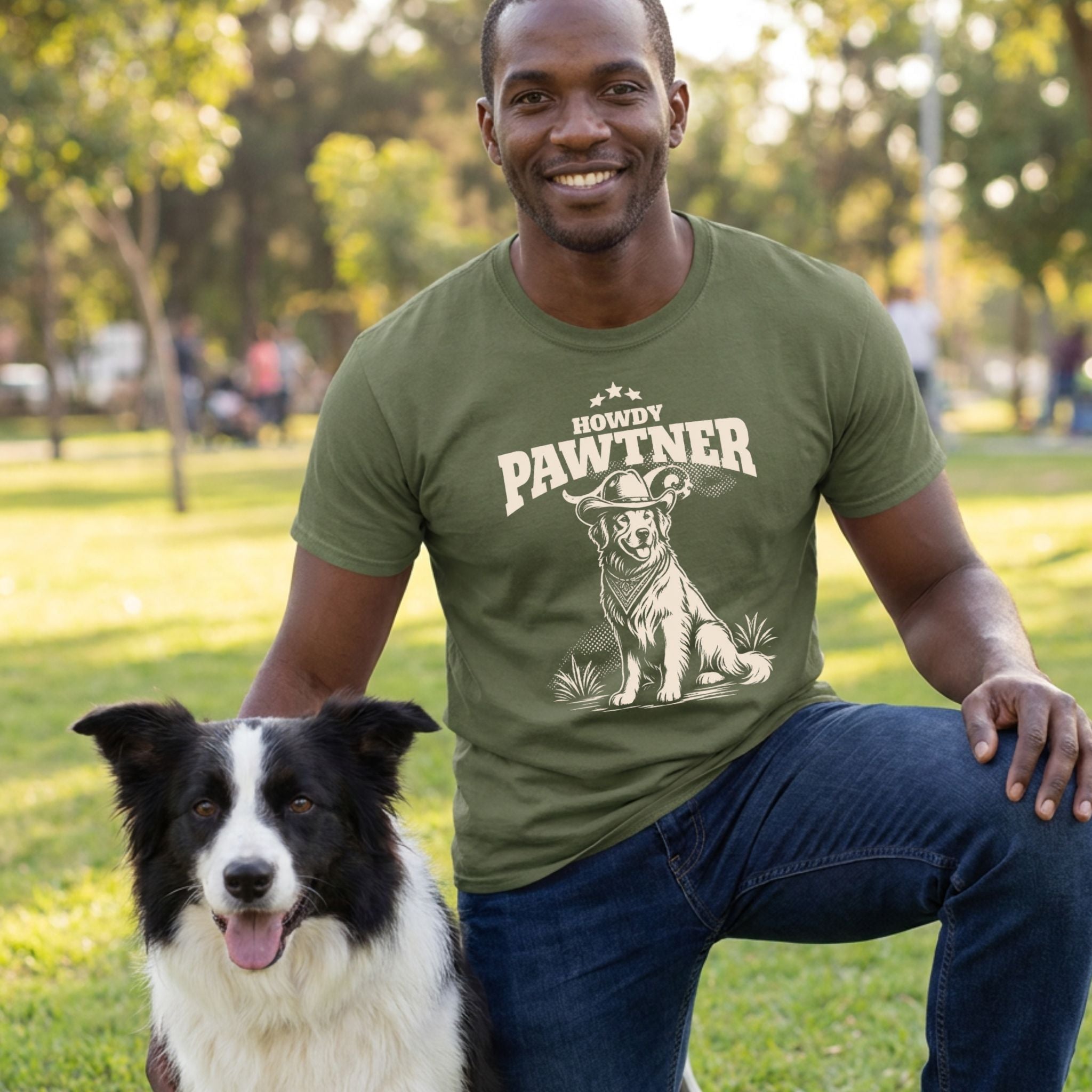 Man wearing an olive green Howdy Pawtner graphic t-shirt featuring a dog in a cowboy hat while kneeling next to a border collie.