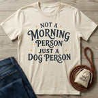 Cream-colored crew neck t-shirt featuring the text Not a Morning Person Just a Dog Person in dark blue vintage-style lettering.