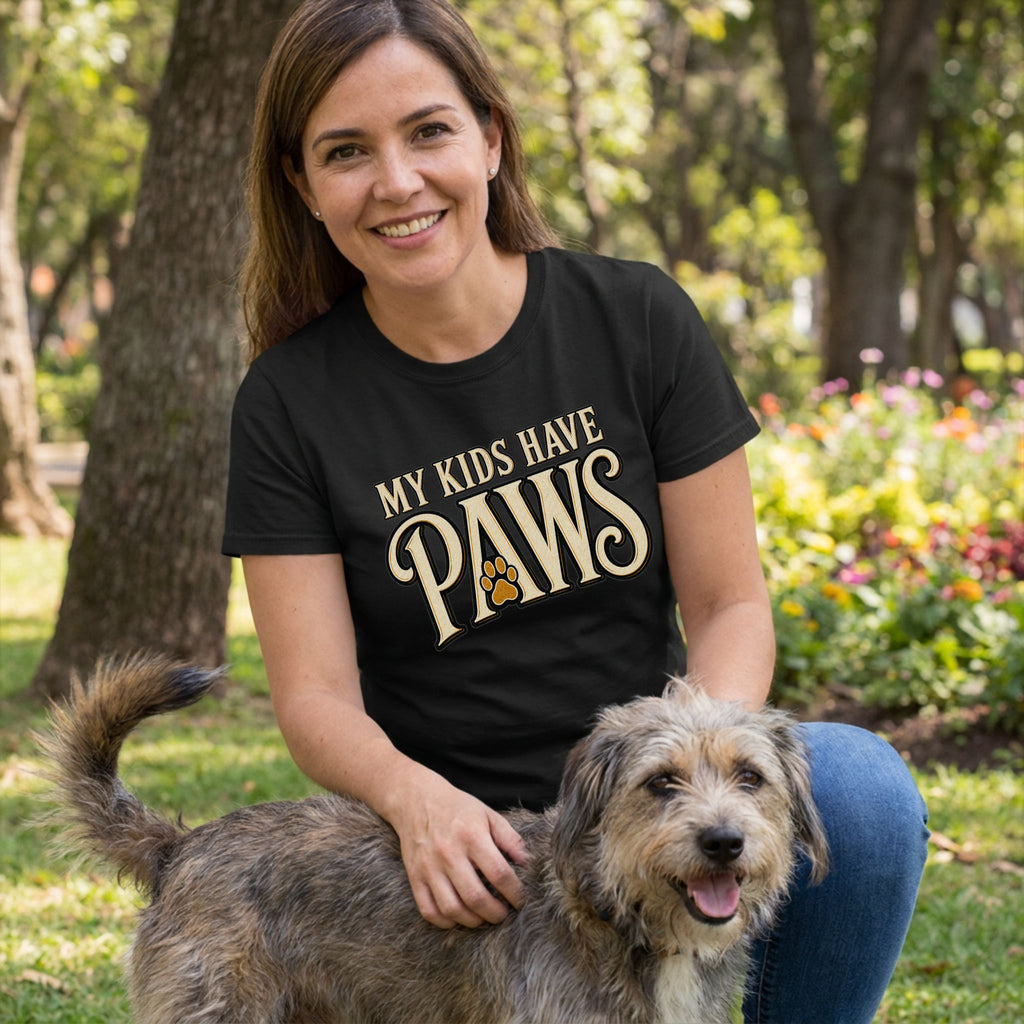 Woman wearing a black crewneck t-shirt with My Kids Have Paws text and a paw print graphic, kneeling outdoors with a dog.