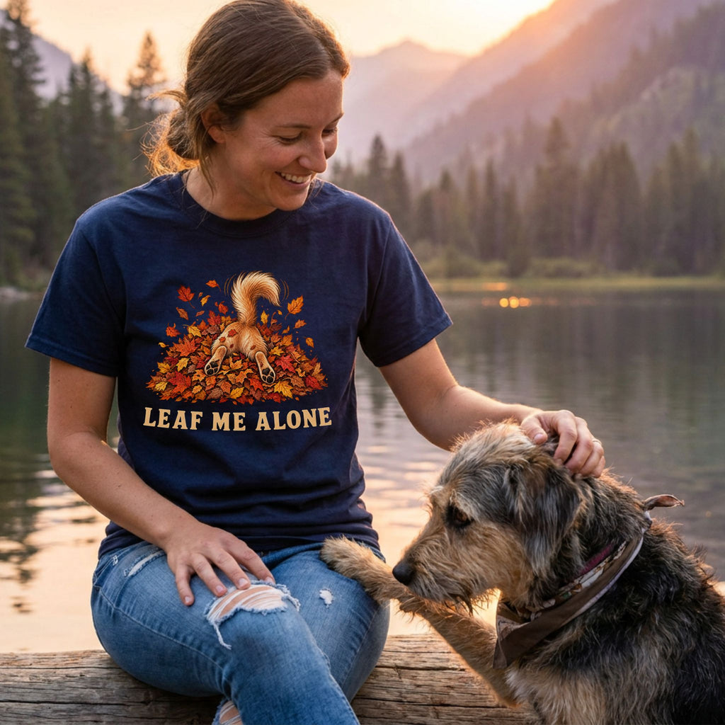 Woman wearing a navy blue cotton t-shirt featuring a dog diving into autumn leaves with the text Leaf Me Alone.