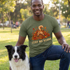 Man wearing an olive green crewneck t-shirt featuring a dog diving into autumn leaves with the text Leaf Me Alone.