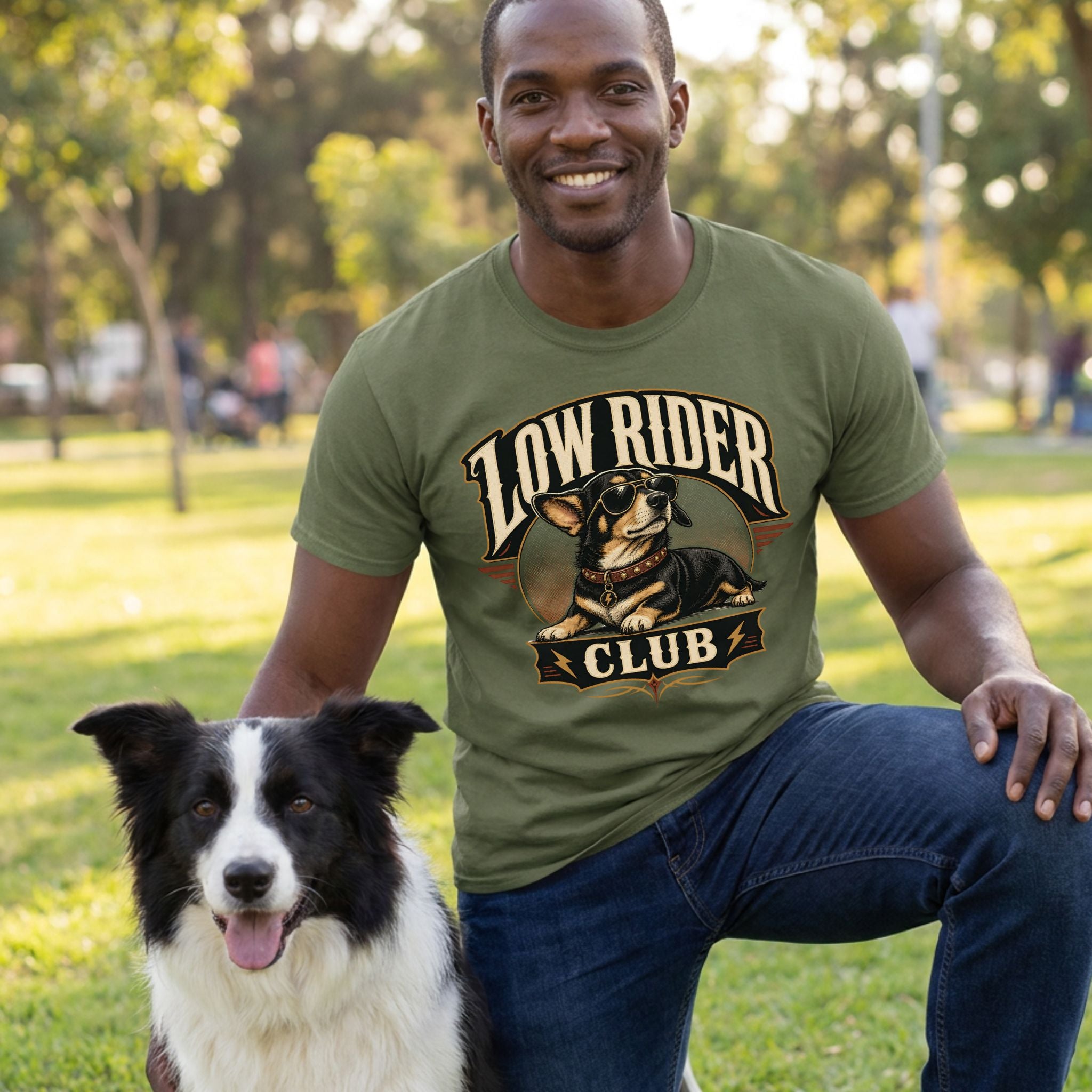 Man wearing an olive green Low Rider Club t-shirt featuring a graphic of a cool dog in sunglasses, kneeling in a park.