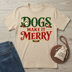 Beige crewneck T-shirt with vintage-style red and green Dogs Make It Merry holiday lettering, holly, and paw print.