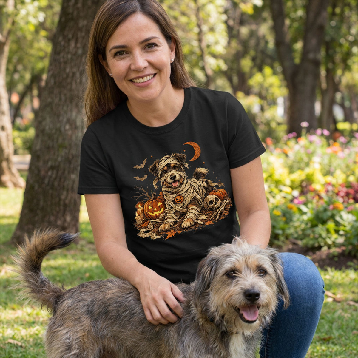Woman wearing a black t-shirt with a graphic of a dog dressed as a mummy among jack-o'-lanterns and a skull.
