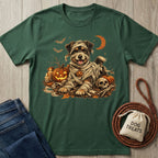 A dark green short-sleeve t-shirt with a Halloween dog graphic, styled in a flat-lay on a light wood background with jeans, a rope, and a small bag labeled 'DOG TREATS'.