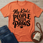 Orange crewneck t-shirt with black My Kind of People Have Paws text and a paw print graphic on a wooden background.