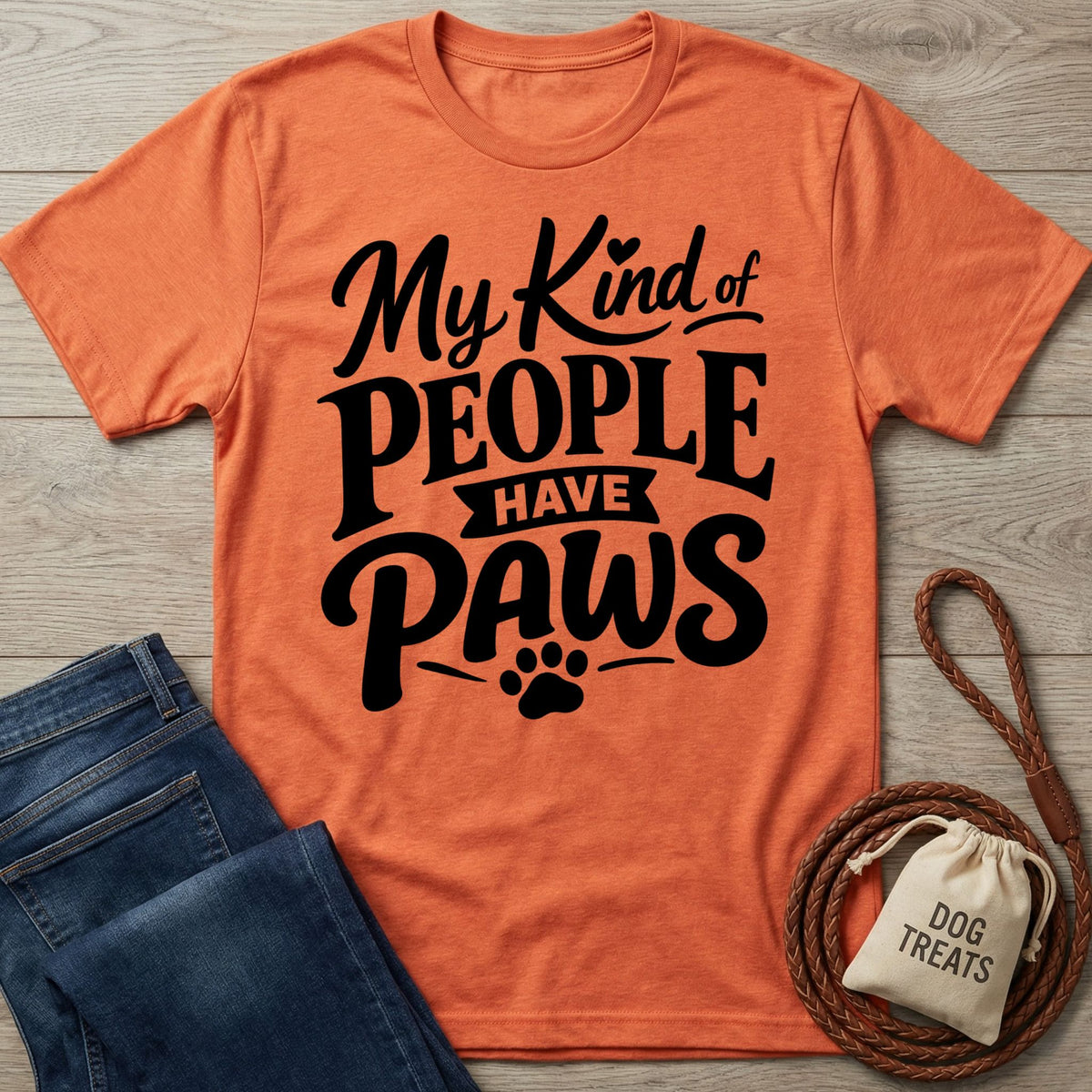 Orange crewneck t-shirt with black My Kind of People Have Paws text and a paw print graphic on a wooden background.