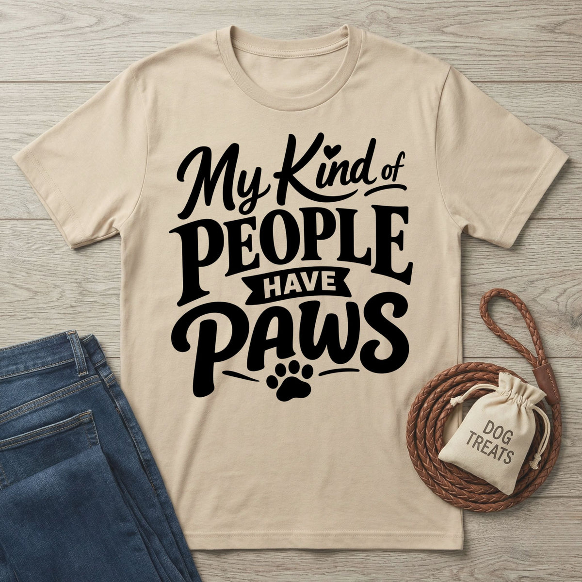 Beige crewneck t-shirt with My Kind of People Have Paws text, displayed with blue jeans and a dog treat bag on wood.
