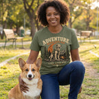 Woman wearing an olive green crewneck t-shirt with a dog hiking graphic, kneeling in a park beside a corgi.