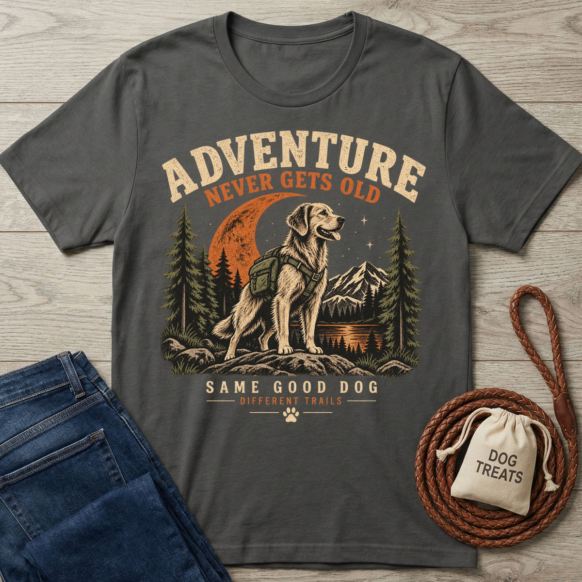 Charcoal grey graphic t-shirt featuring a hiking dog illustration, mountain scenery, and Adventure Never Gets Old text.