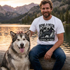 Man wearing a white graphic t-shirt with a Howl-o-ween dog design, sitting on a log by a lake with a fluffy husky.