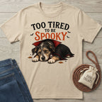 Beige crewneck t-shirt featuring a sleepy dog in a vampire cape with the text Too Tired To Be Spooky.