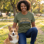Woman in an olive green "Official Poop Bag Carrier" tee with a Corgi in a park.