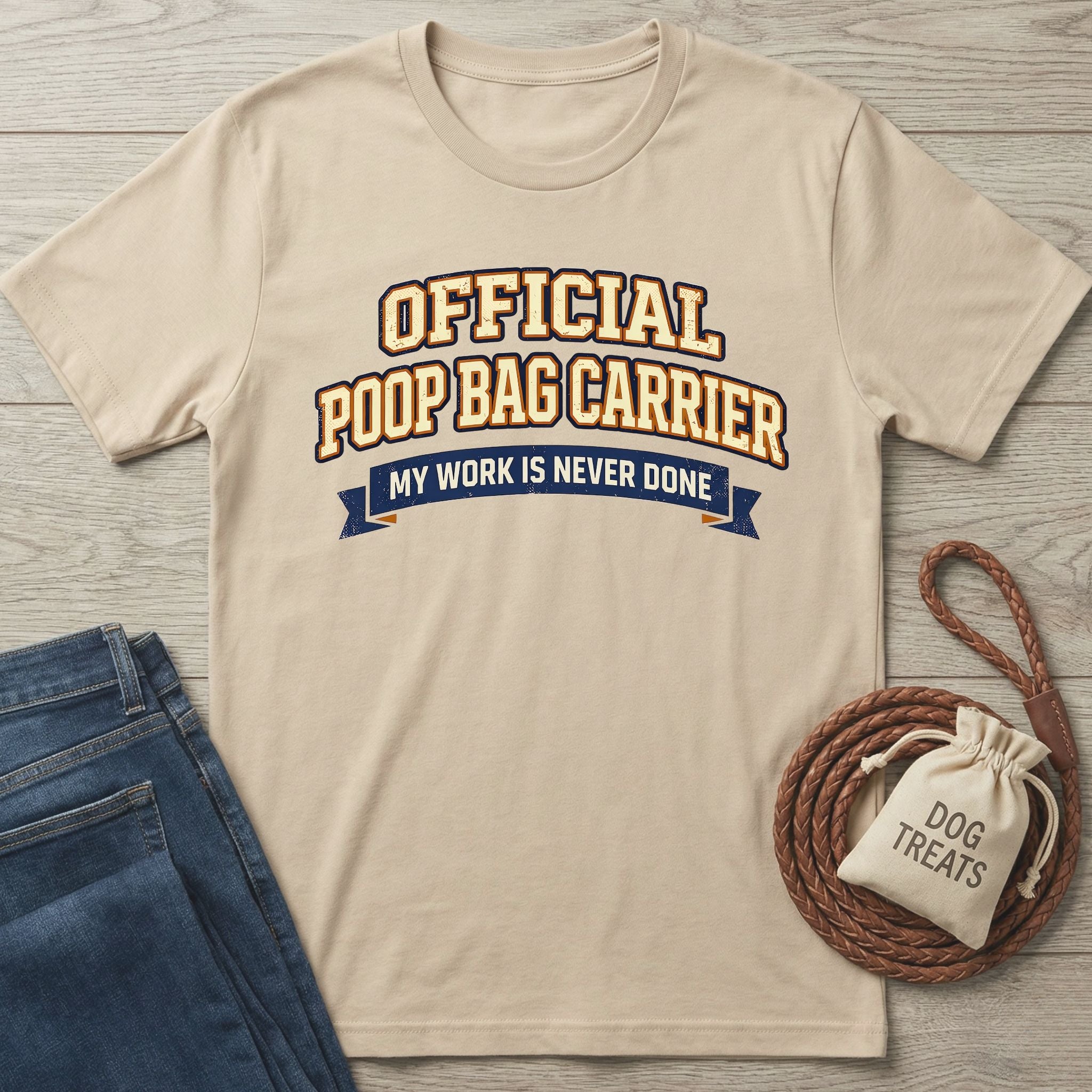 Tan Gildan Softstyle® t-shirt with "Official Poop Bag Carrier" text, next to jeans and dog treats.