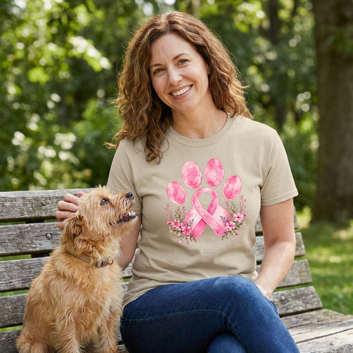 Woman wearing a beige T-shirt featuring a watercolor pink ribbon and paw print design with floral accents while sitting with a dog.