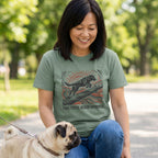 Woman wearing an olive green t-shirt with a woodblock-style graphic of a dog jumping over a log and sunburst design.