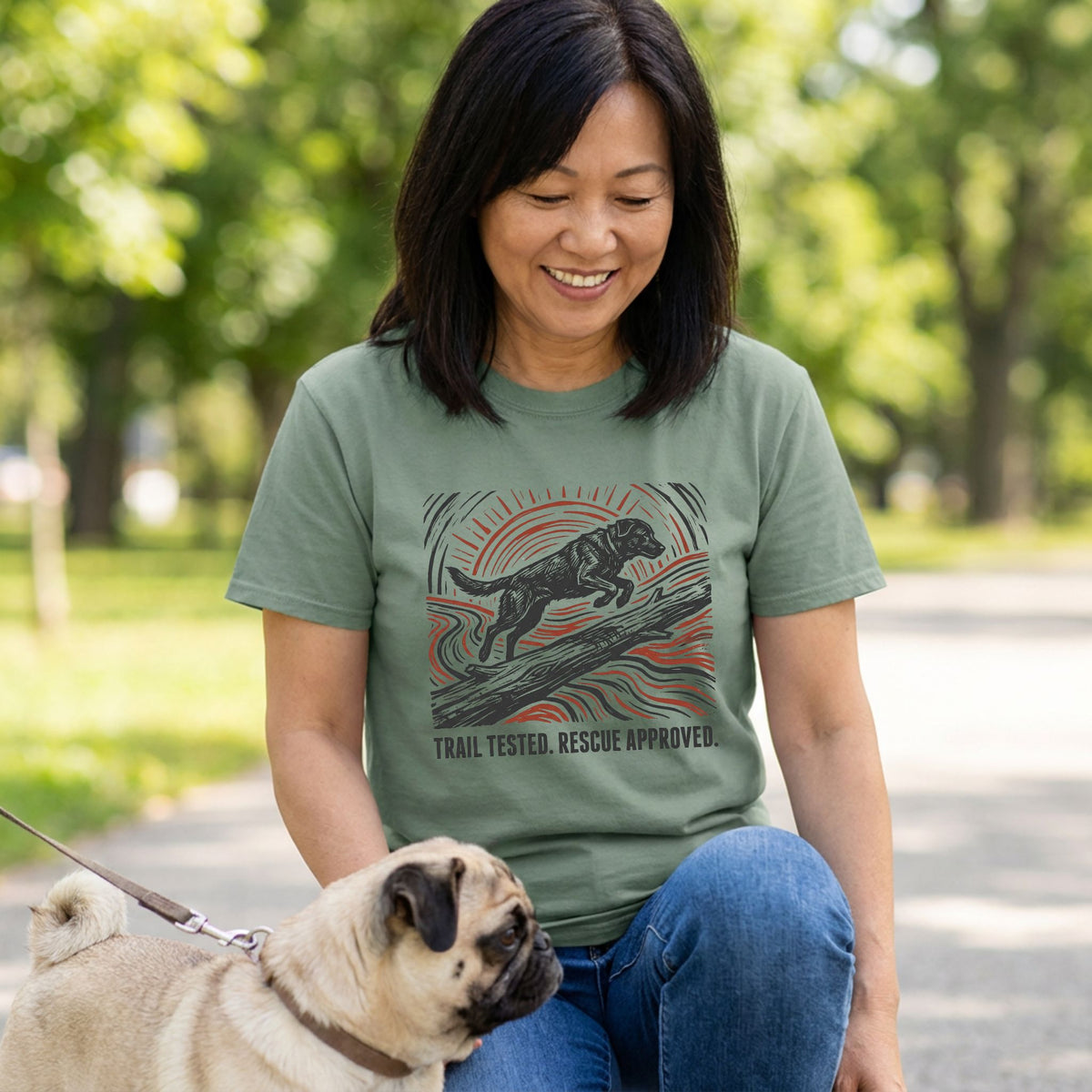 Woman wearing an olive green t-shirt with a woodblock-style graphic of a dog jumping over a log and sunburst design.