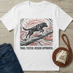 White t-shirt featuring a black and red woodblock-style print of a dog jumping over a log with the text Trail Tested. Rescue Approved.