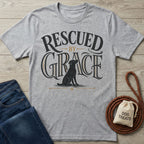 Grey crewneck t-shirt featuring a black dog illustration and Rescued By Grace typography on a wooden background.