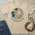 Beige "Rescued & Rooted" Gildan Softstyle® t-shirt with a dog, monstera leaves, and flowers.