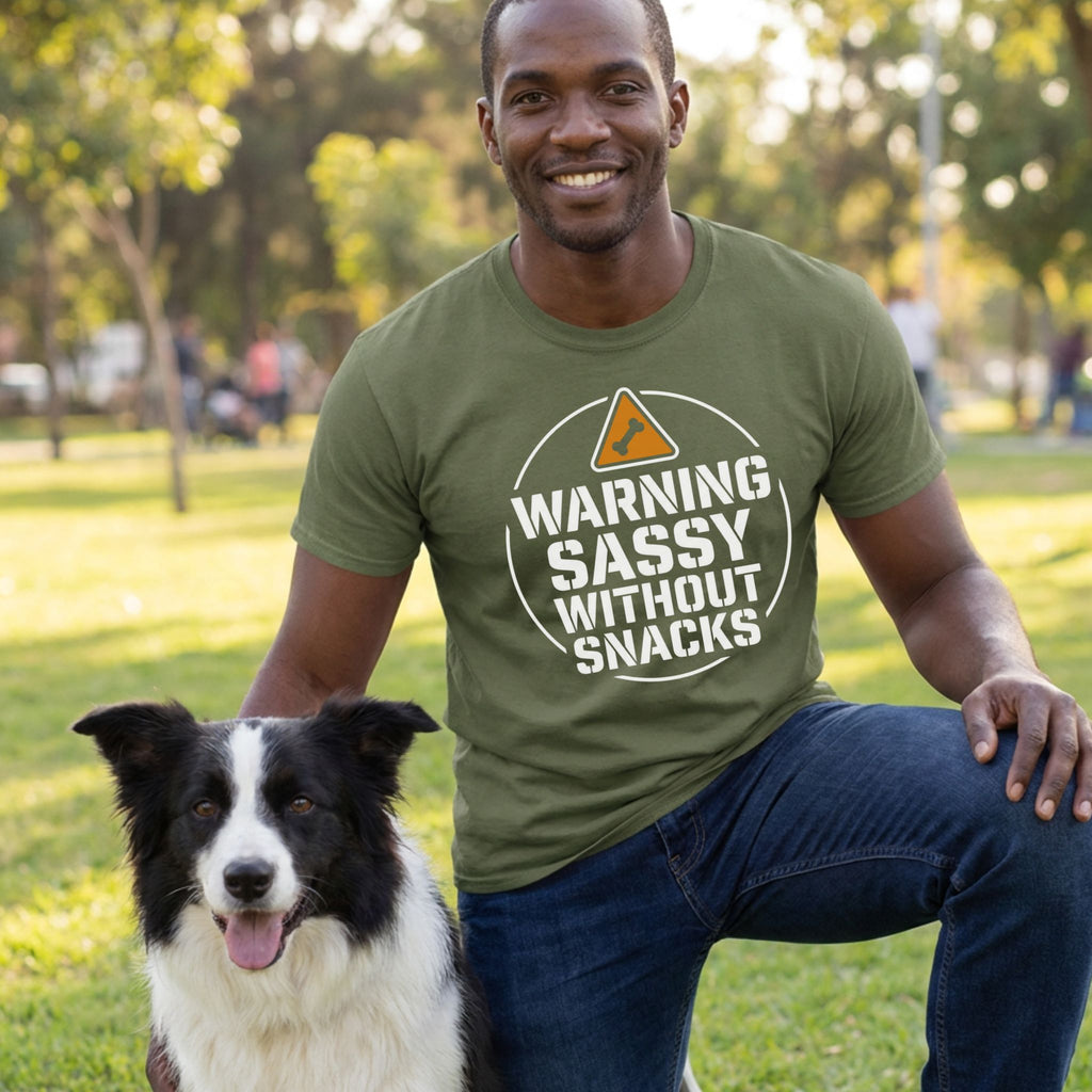 Man in an olive green "Warning Sassy Without Snacks" t-shirt kneeling beside a black and white dog.