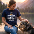 Woman in navy "Warning Sassy Without Snacks" t-shirt petting a dog by a lake at sunset.