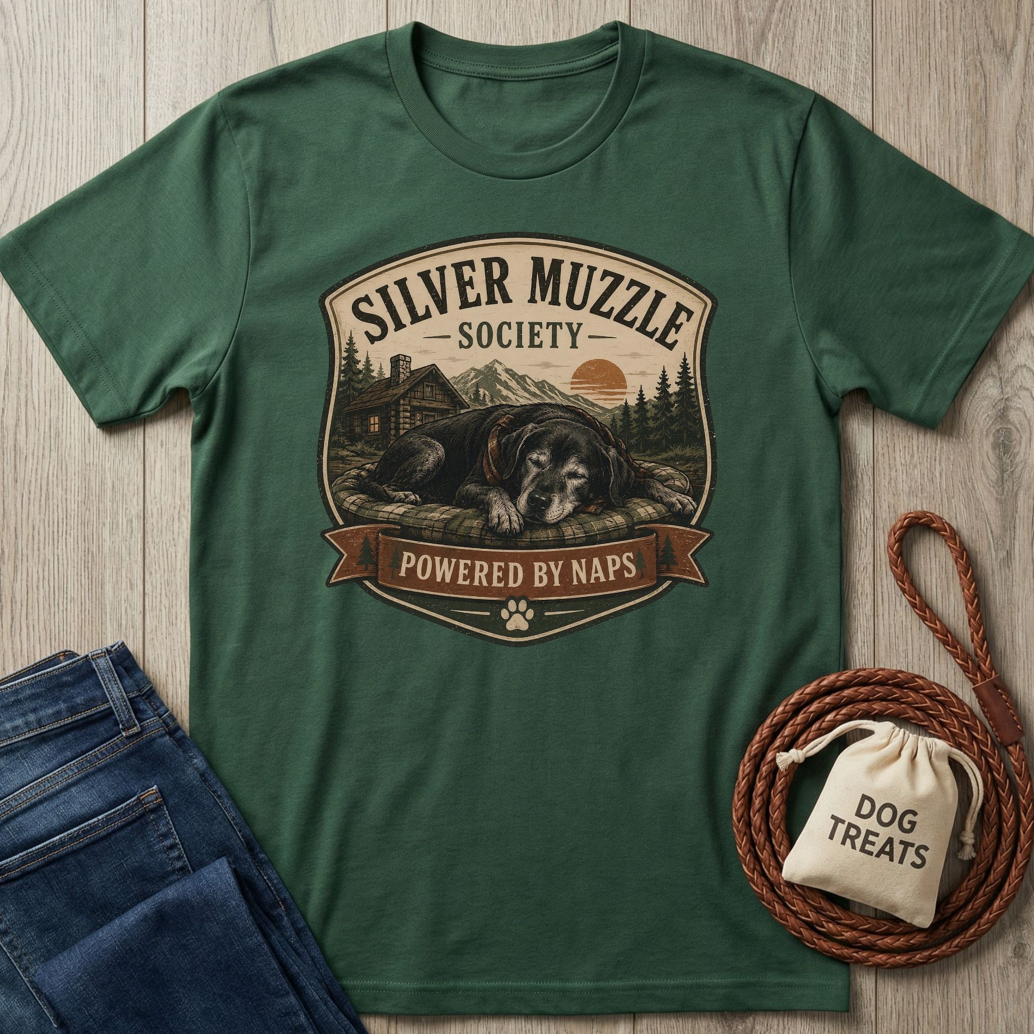 Dark green "Silver Muzzle Society" t-shirt with a sleeping senior dog graphic, next to jeans and dog treats.