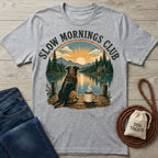 Grey crewneck t-shirt featuring a dog and coffee mug on a dock overlooking a lake, mountains, and sunrise.