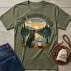 Olive green crewneck t-shirt featuring a graphic of a dog and coffee mug on a dock overlooking a mountain lake sunrise.