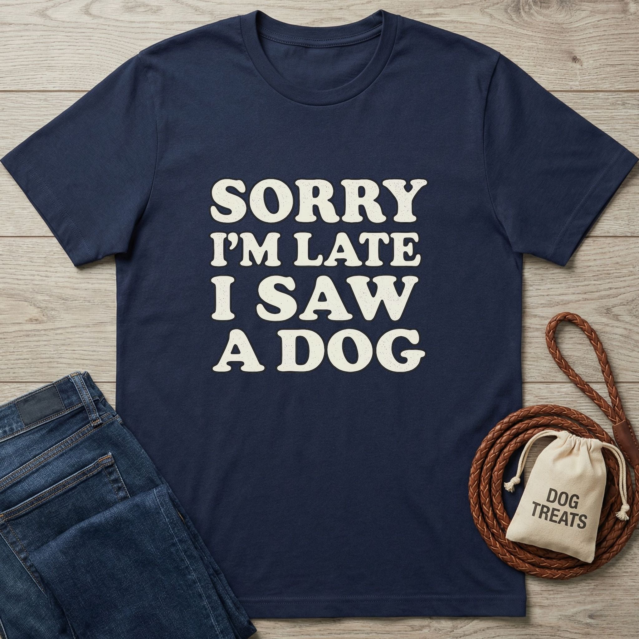 Navy blue "Sorry I'm Late I Saw A Dog" graphic tee, folded beside jeans, a dog leash, and treat bag.