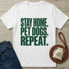 White Gildan Softstyle t-shirt with "STAY HOME. PET DOGS. REPEAT." in green text, next to jeans and a dog leash.