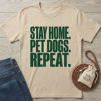 Beige Gildan Softstyle® t-shirt with "STAY HOME. PET DOGS. REPEAT." in dark green text, beside jeans and dog treats.