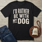 Black crewneck t-shirt with distressed white text reading I'D RATHER BE WITH MY DOG, laid on a wood surface with denim.