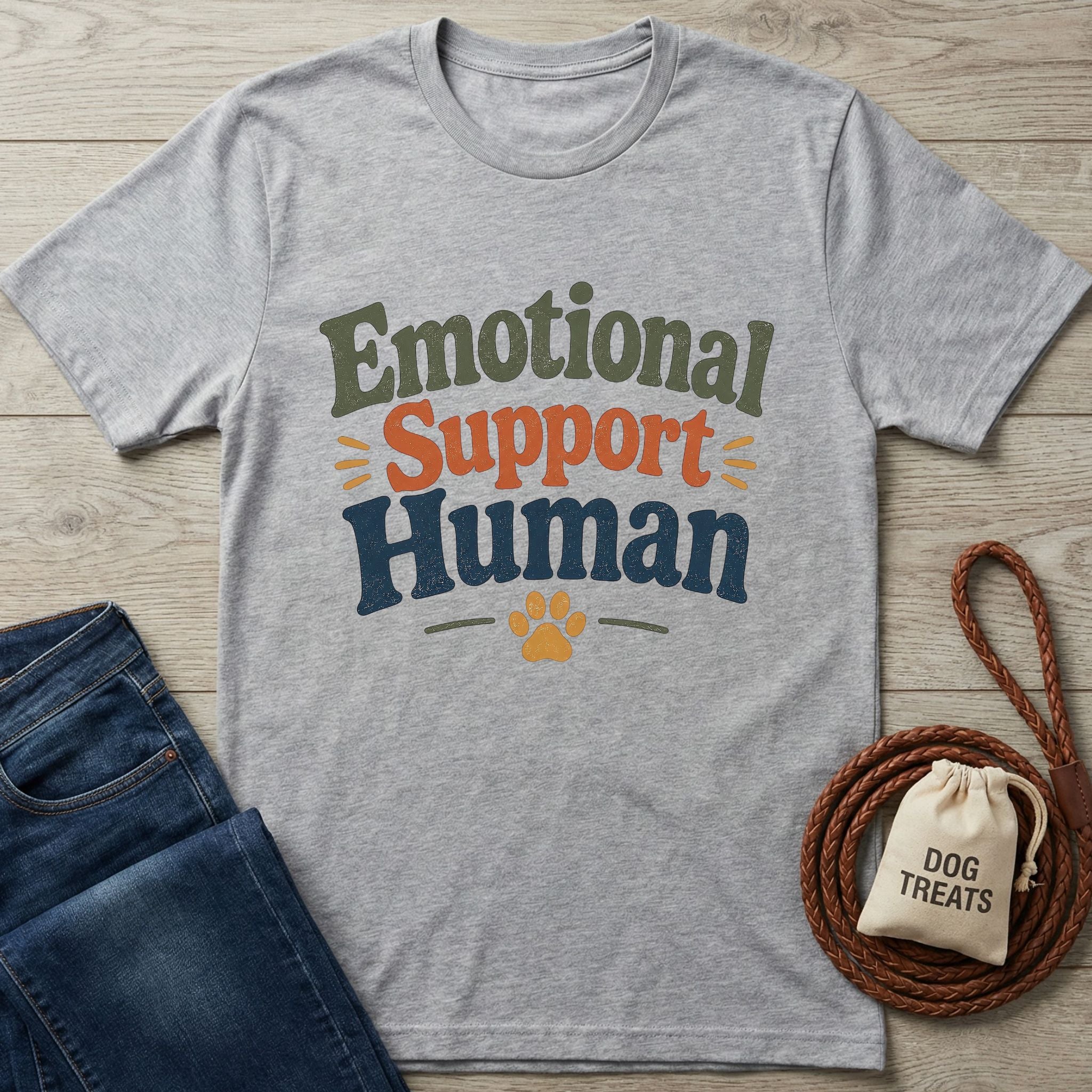 Heather gray "Emotional Support Human" t-shirt with a paw print, next to jeans and dog treats.