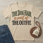 Beige graphic T-shirt featuring vintage-style text reading The Dog Hair is part of The OUTFIT, laid on a wooden surface.