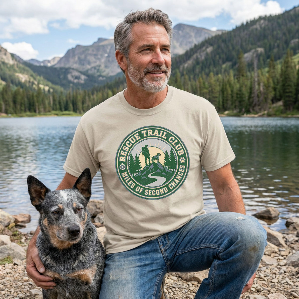 Man in a beige "Rescue Trail Club" tee with a dog, mountains, and lake in the background.