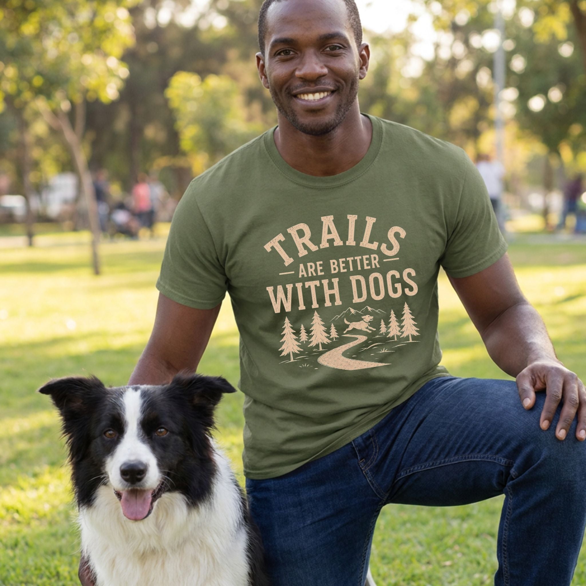Man in an olive green "Trails Are Better With Dogs" T-shirt with a mountain trail graphic, kneeling beside a Border Collie.