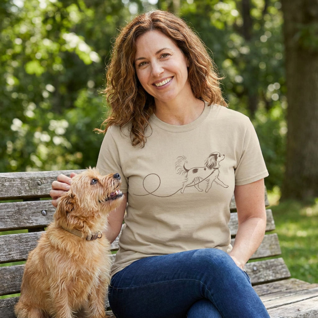Woman wearing a tan crewneck t-shirt with a minimalist brown line drawing of a dog on a leash, sitting on a park bench.
