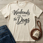 Cream-colored crewneck t-shirt with black Weekends Are For The Dogs script text, laid flat with jeans and a leather leash.