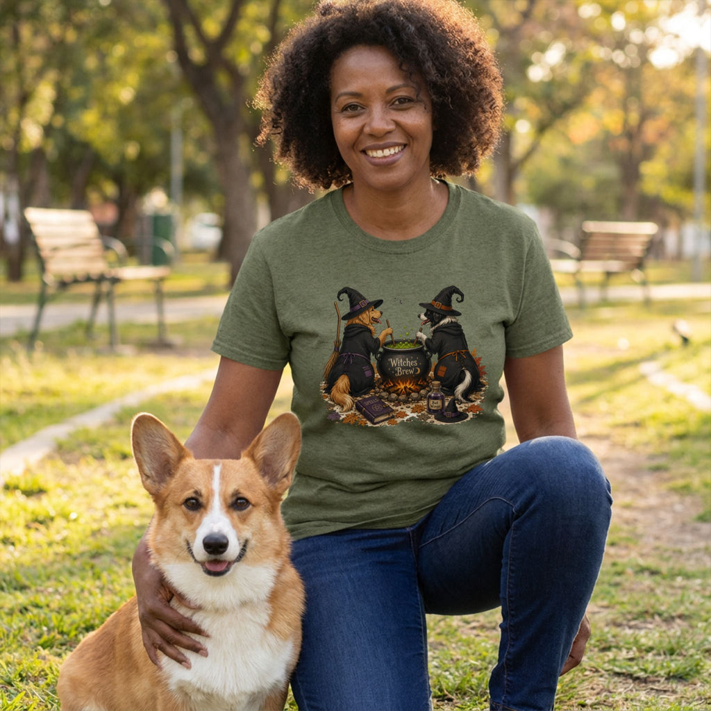 Woman wearing an olive green crewneck T-shirt featuring two dogs in witch hats stirring a bubbling cauldron graphic.