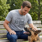 Man in a heather gray "Working Hard For My Rescue" t-shirt petting a German Shepherd on a park bench.