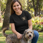 Woman wearing a black vintage-style Every Dog Society band t-shirt with a paw print graphic, kneeling outdoors with a dog.